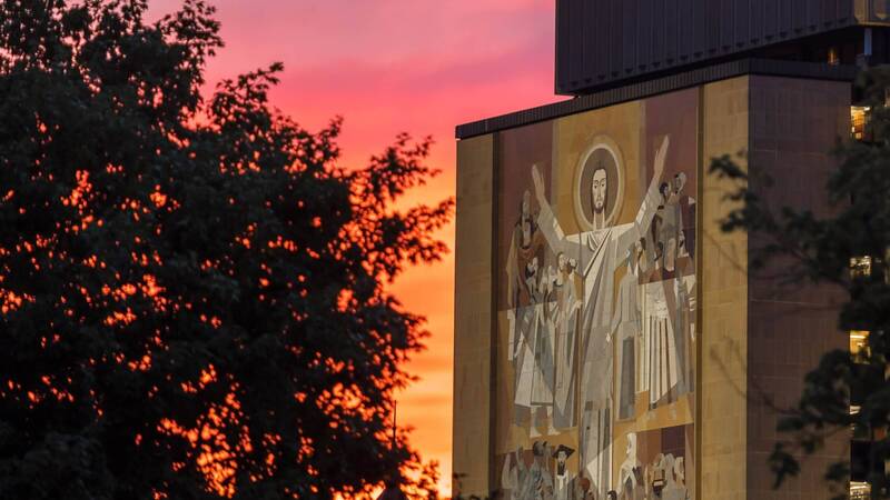 Vibrant red sunset behind Hesburgh Library's Word of Life mural.